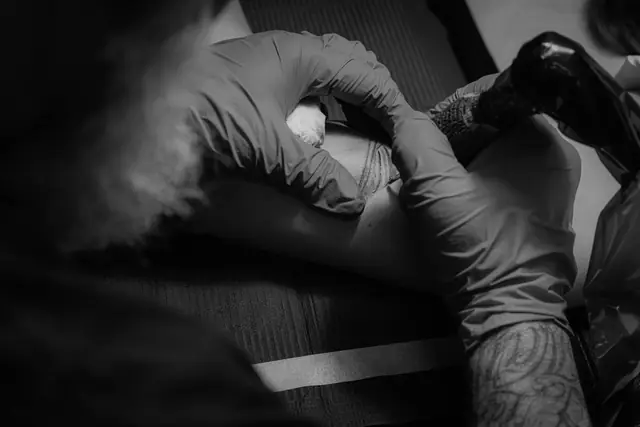 Mains d’un tatoueur au travail, en noir et blanc